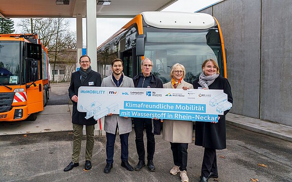 Fünf Verantwortliche stehen mit einem Plakakat vor einem Bus und einem Abfallsammelfahrzeug an der neuen Wasserstkfftankstelle.